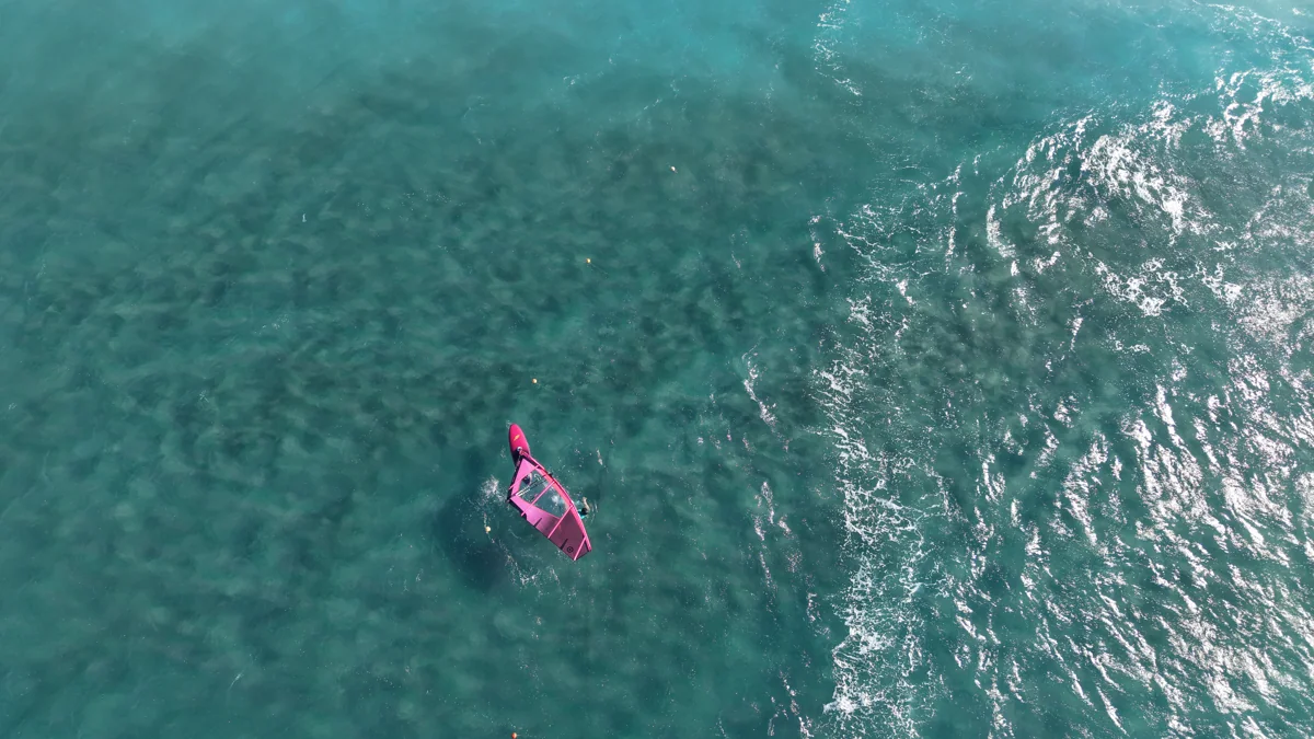 A windsurfer turning in clear turquoise water, seen from above