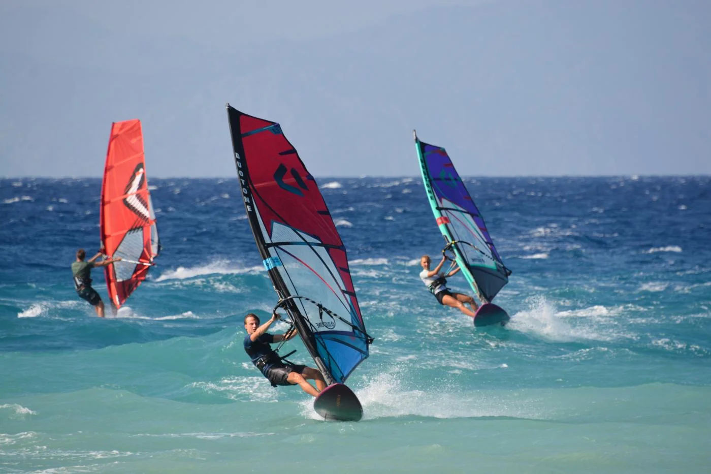 Three windsurfers sailing in the open-water chop of Rhodes